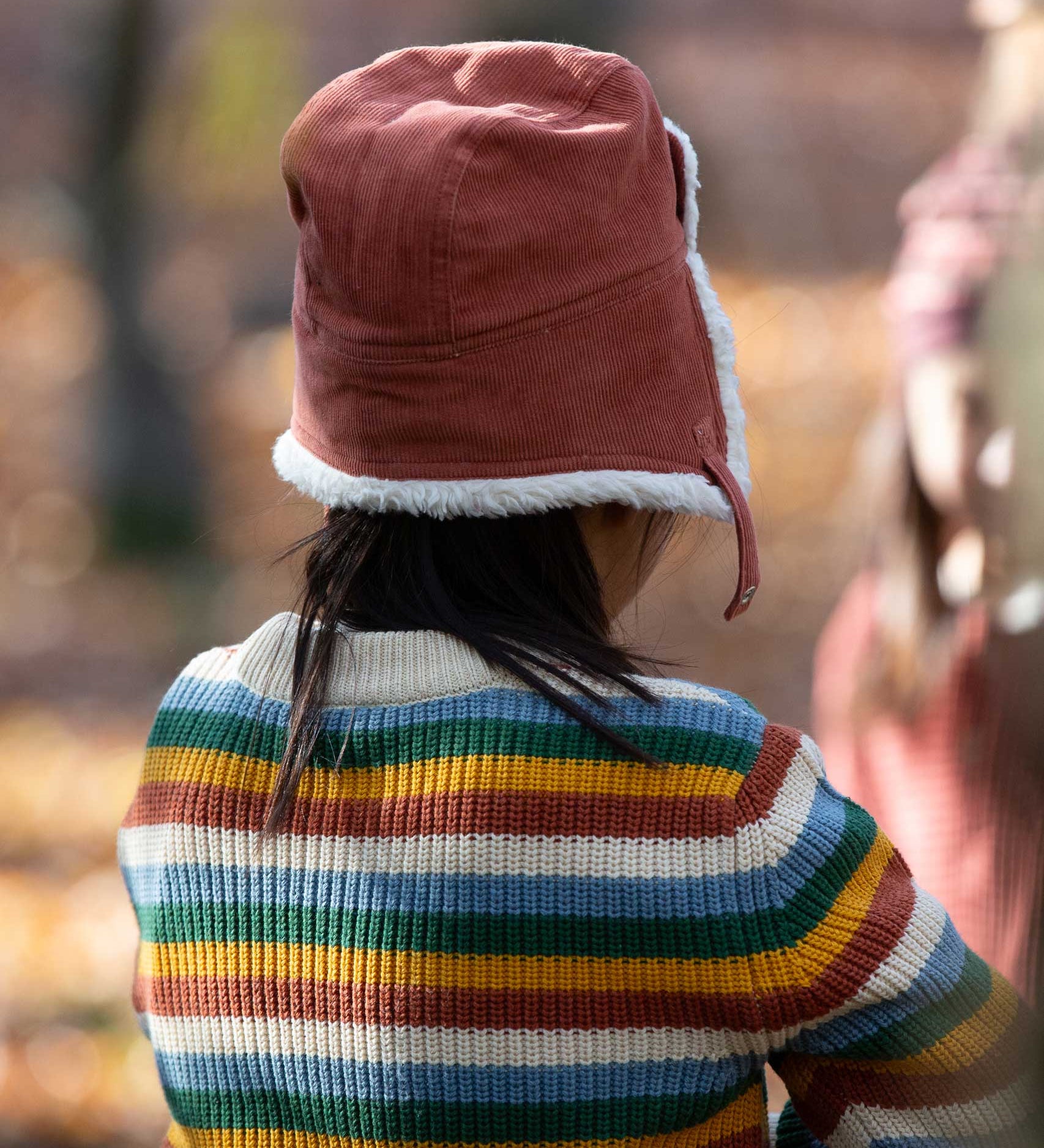 A child wearing the Little Green Radicals Ginger orange coloured Children's Sherpa Fleece Cosy Hat. This hat is a part of a wide range of organic cotton clothing and accessories for children available here at Babipur. 