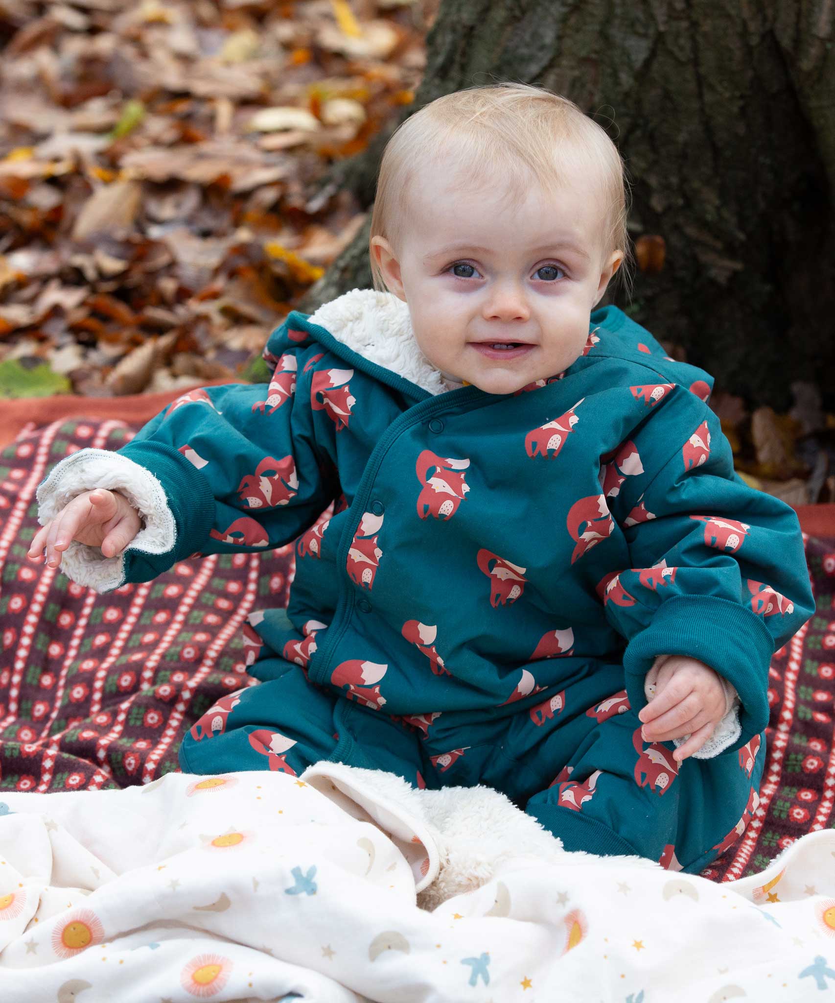 A baby wearing the Little Green Radicals Sherpa Fleece Snowsuit , a Organic Cotton suit with a Red Foxes all over print on a dark green background. This lined snowsuit is a part of a wide range of organic cotton clothing for children available here at Babipur. 