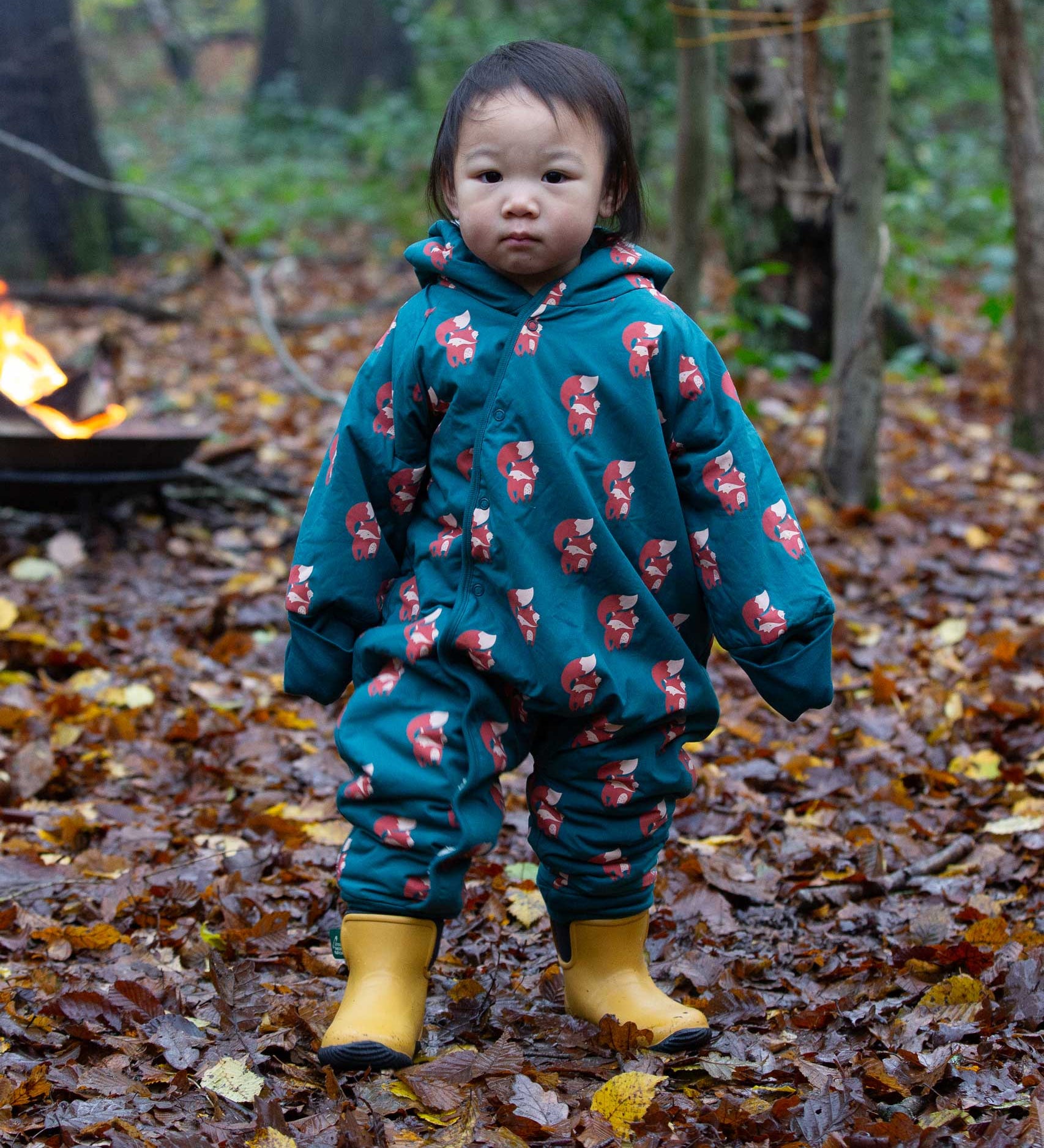 A child wearing the Little Green Radicals Sherpa Fleece Snowsuit , a Organic Cotton suit with a Red Foxes all over print on a dark green background. This lined snowsuit is a part of a wide range of organic cotton clothing for children available here at Babipur. 
