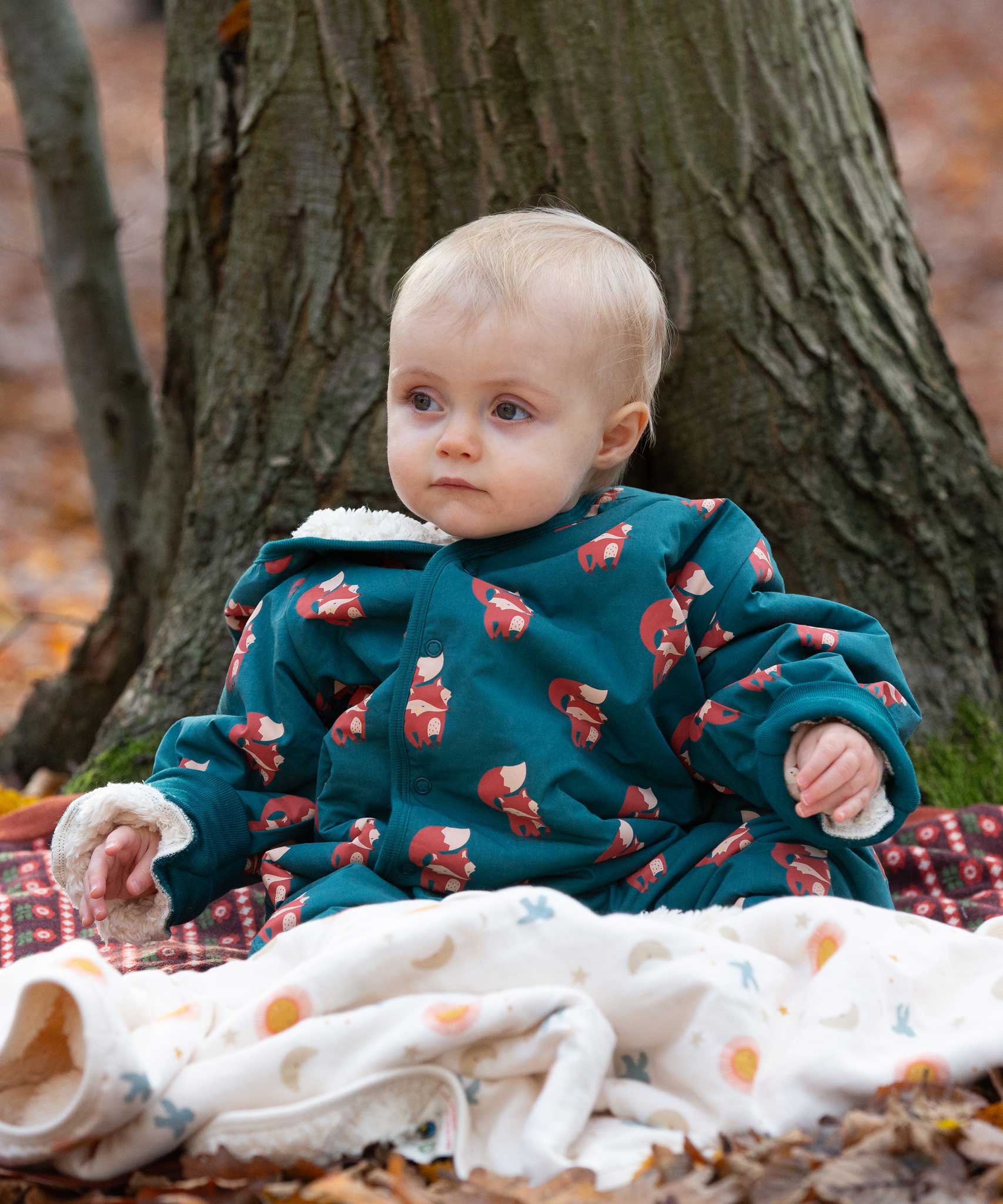A baby wearing the Little Green Radicals Sherpa Fleece Snowsuit , a Organic Cotton suit with a Red Foxes all over print on a dark green background. This lined snowsuit is a part of a wide range of organic cotton clothing for children available here at Babipur. 