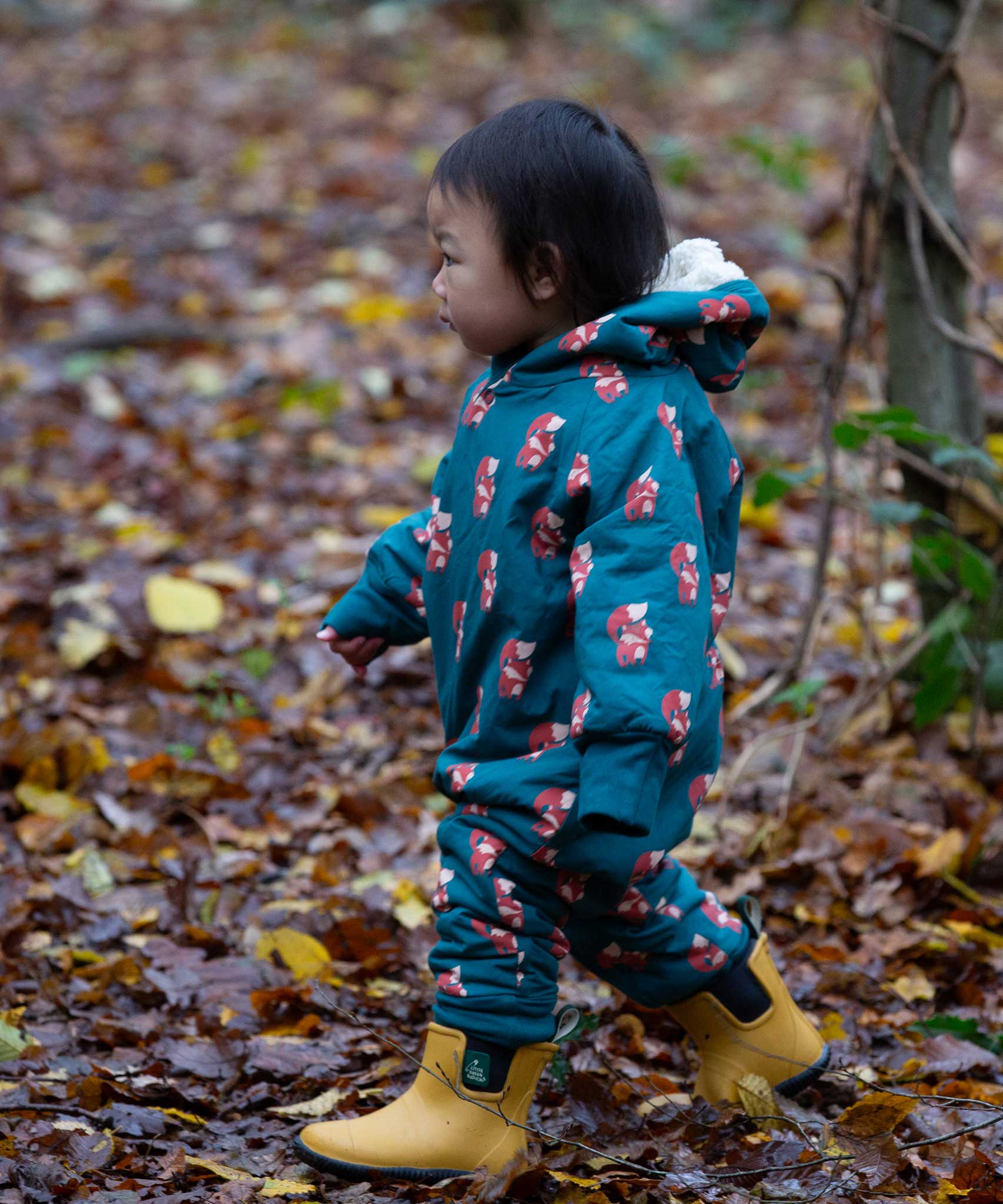 A child wearing the Little Green Radicals Sherpa Fleece Snowsuit , a Organic Cotton suit with a Red Foxes all over print on a dark green background. This lined snowsuit is a part of a wide range of organic cotton clothing for children available here at Babipur. 