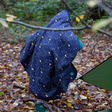 A child walking through a forest wearing a Little Green Radicals dark night print Organic Sherpa Hooded Baby Blanket over their head.  A GOTS organic cotton navy blanket with a starry night print and a brand logo patch on the corner. Features a white sherpa style fleece lining. This blanket is a part of a wide range of organic cotton clothing and accessories for children available here at Babipur. 
