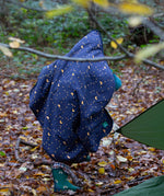 A child walking through a forest wearing a Little Green Radicals dark night print Organic Sherpa Hooded Baby Blanket over their head.  A GOTS organic cotton navy blanket with a starry night print and a brand logo patch on the corner. Features a white sherpa style fleece lining. This blanket is a part of a wide range of organic cotton clothing and accessories for children available here at Babipur. 
