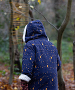 A view of the back of a child wearing the Little Green Radicals Kids Dark Night design Organic Sherpa lined Toasty Coat. The child has the hood up. This warm coat is navy with a yellow moon and stars print all over with a white sherpa fleece lining. This coat is a part of a wide range of organic cotton clothing for children available here at Babipur. 