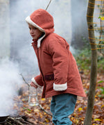A child wearing the Little Green Radicals Kids Organic Sherpa Toasty Coat in a ginger colourway. This warm orange coloured jacket is part of a wide range of organic cotton clothing for children available here at Babipur. 