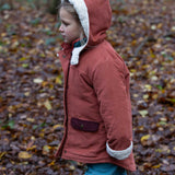 A child wearing the Little Green Radicals Kids Organic Sherpa Toasty Coat in a ginger colourway. This warm orange coloured jacket is part of a wide range of organic cotton clothing for children available here at Babipur. 