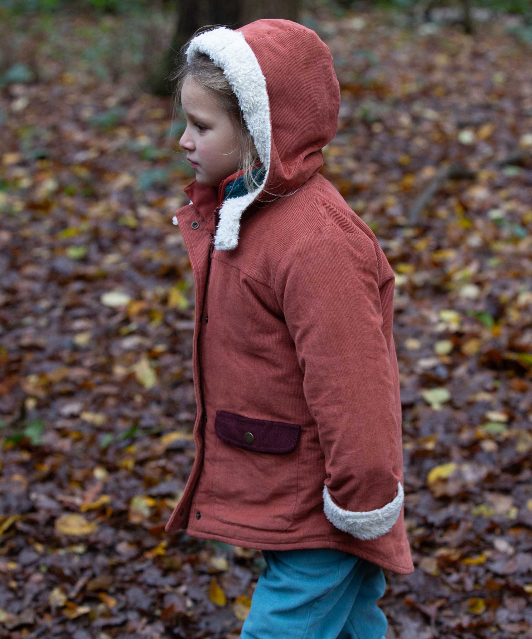 A child wearing the Little Green Radicals Kids Organic Sherpa Toasty Coat in a ginger colourway. This warm orange coloured jacket is part of a wide range of organic cotton clothing for children available here at Babipur. 