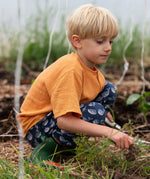 Child wearing the Little Green Radicals navy singing whales print comfy organic cotton joggers with a yellow muslin henley t-shirt.