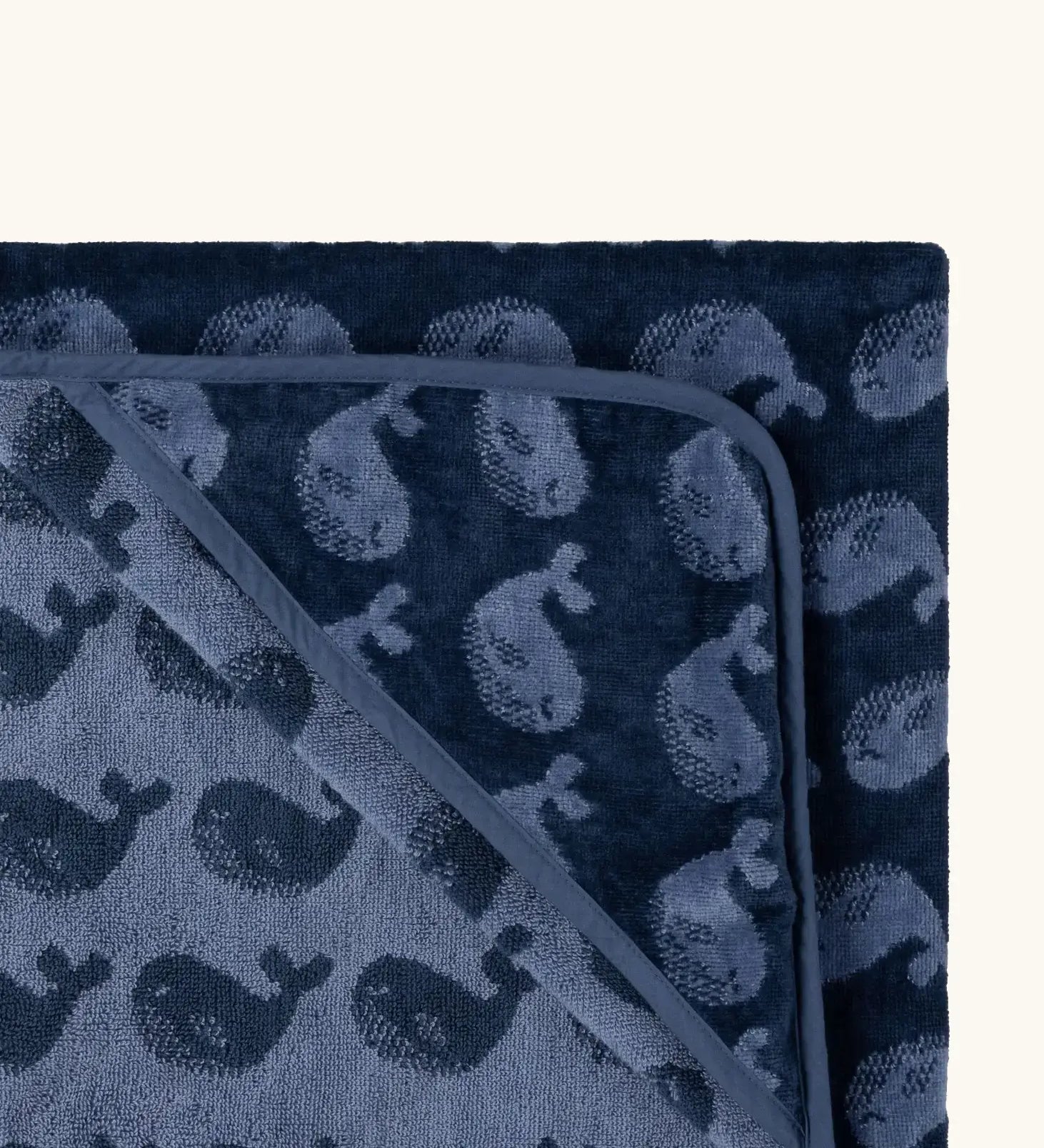 Top corner of Little Green Radicals GOTS organic cotton hooded towel in navy blue with a repeating whale design