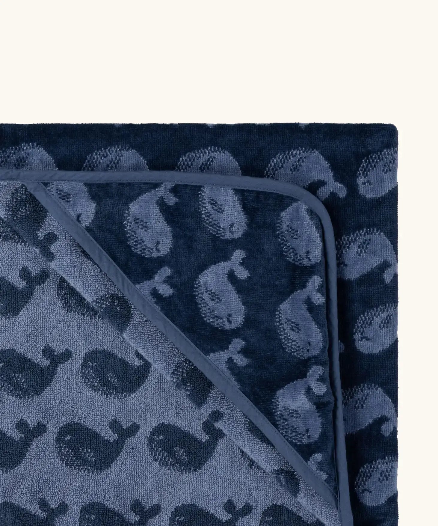 Top corner of Little Green Radicals GOTS organic cotton hooded towel in navy blue with a repeating whale design
