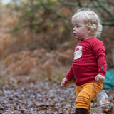Child wearing the Little Green Radicals sleeping swan applique long sleeve organic cotton top in red with yellow gold joggers.