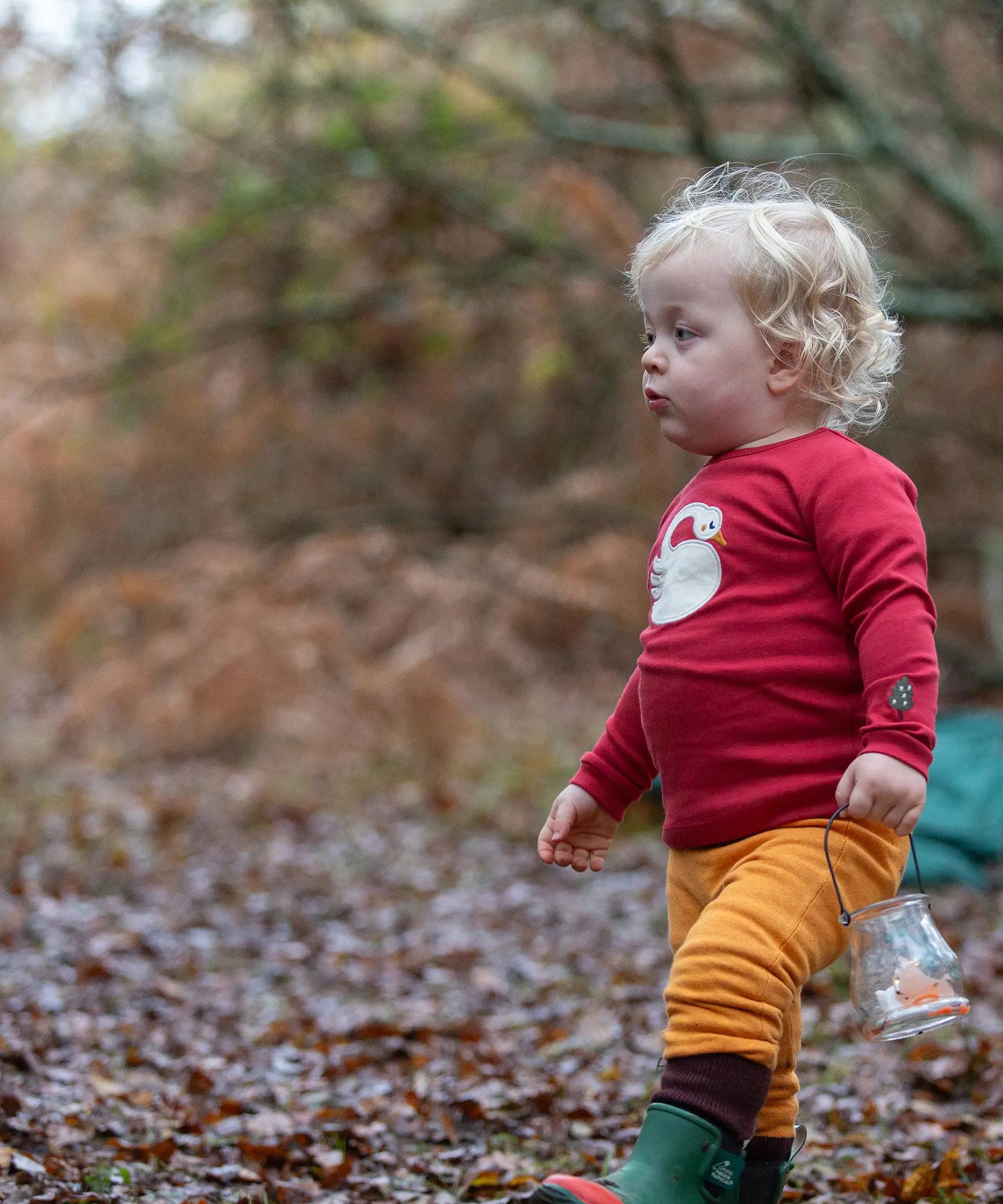 Child wearing the Little Green Radicals sleeping swan applique long sleeve organic cotton top in red with yellow gold joggers.