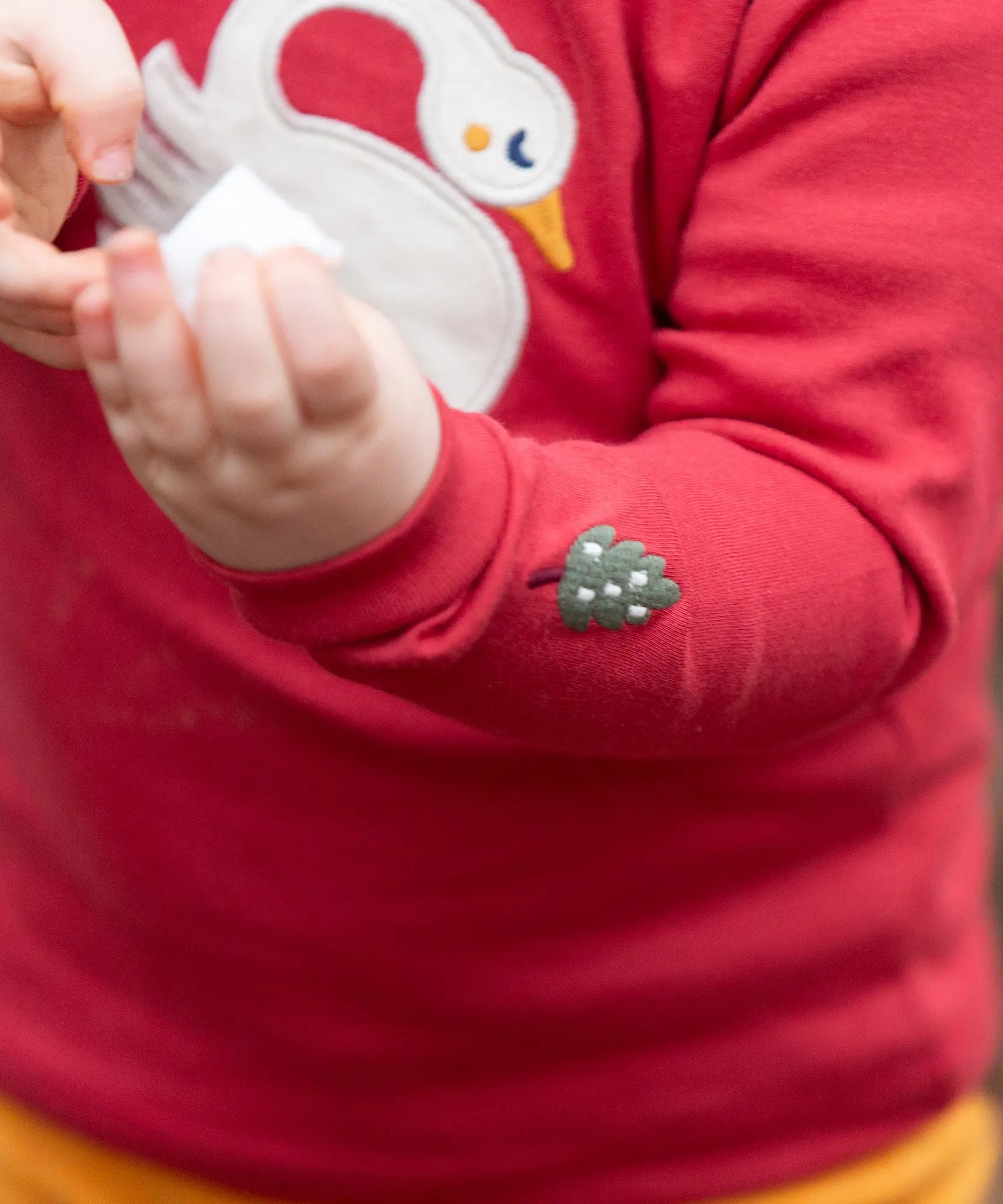 Close up of the little tree embroidery details on the sleeve of the Little Green Radicals sleeping swan applique long sleeve organic cotton top in red.