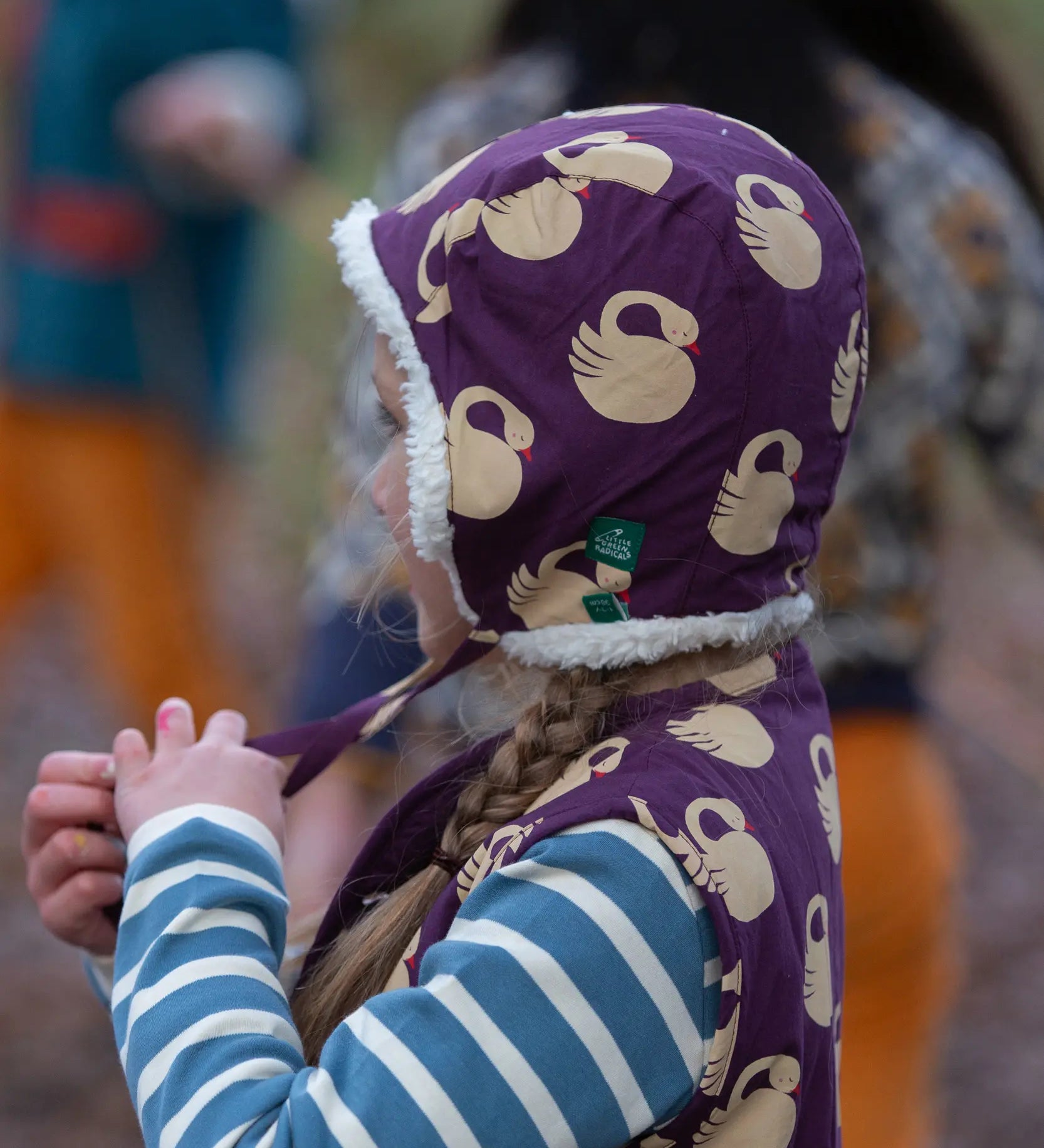 Child wearing a Little Green Radicals  sleeping swans print sherpa fleece lined purple hat.