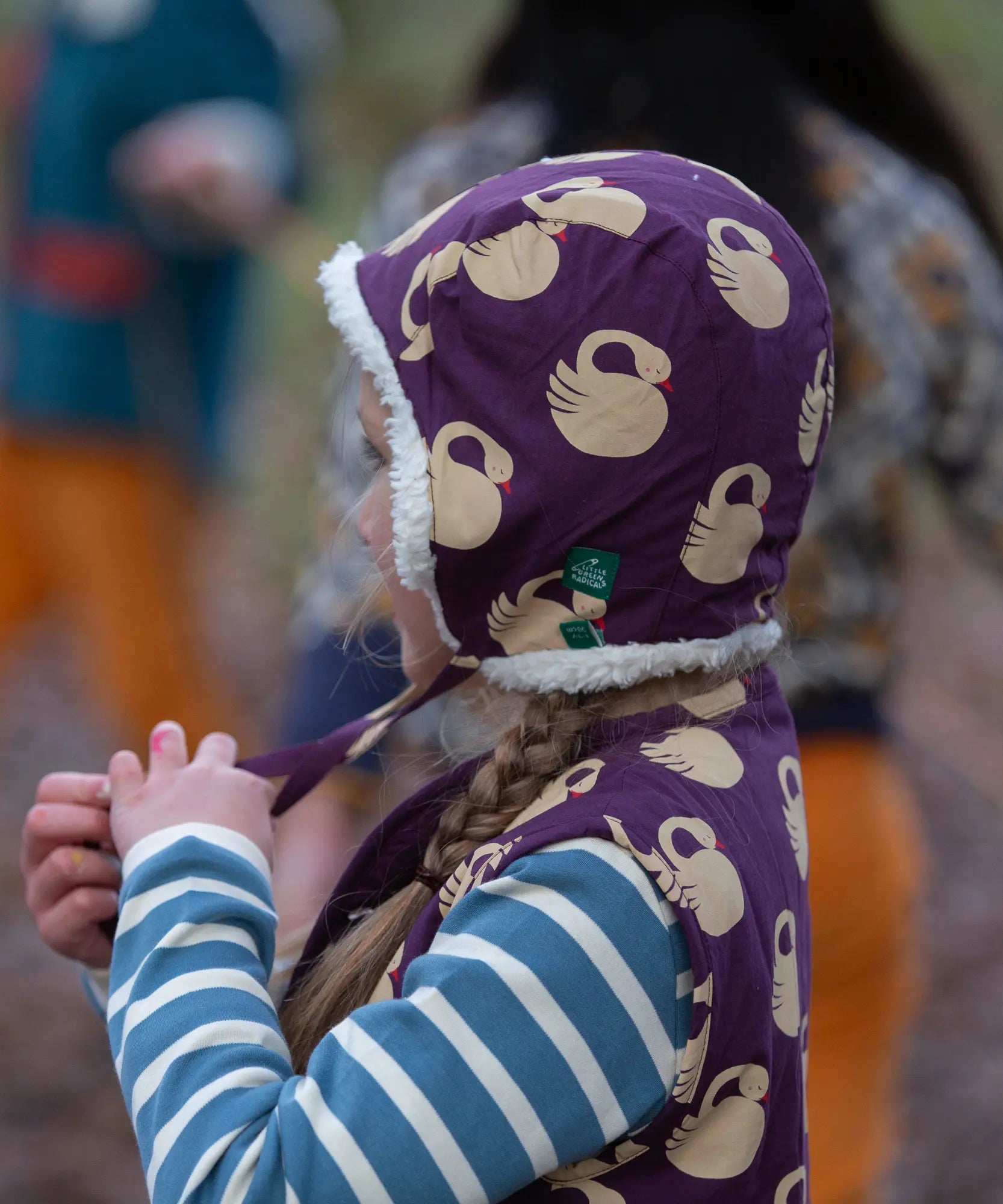 Child wearing a Little Green Radicals  sleeping swans print sherpa fleece lined purple hat.