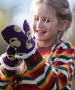 Child wearing Little Green Radicals  sleeping swans print sherpa fleece lined purple mittens with a rainbow striped knitted jumper.