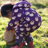 Child wearing the Little Green Radicals purple sleeping swans print sherpa lined snowsuit with red wellington boots.