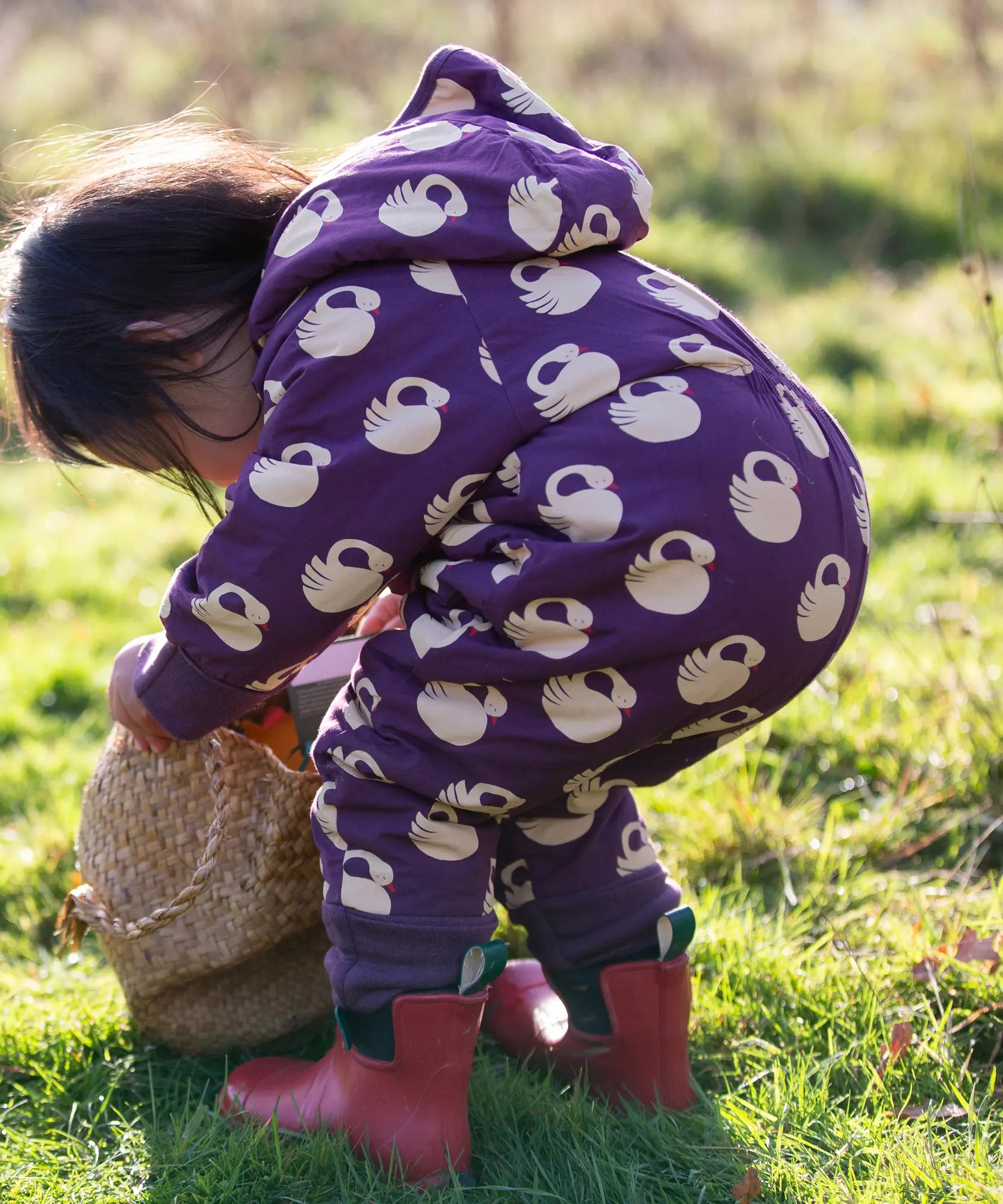 Child wearing the Little Green Radicals purple sleeping swans print sherpa lined snowsuit with red wellington boots.