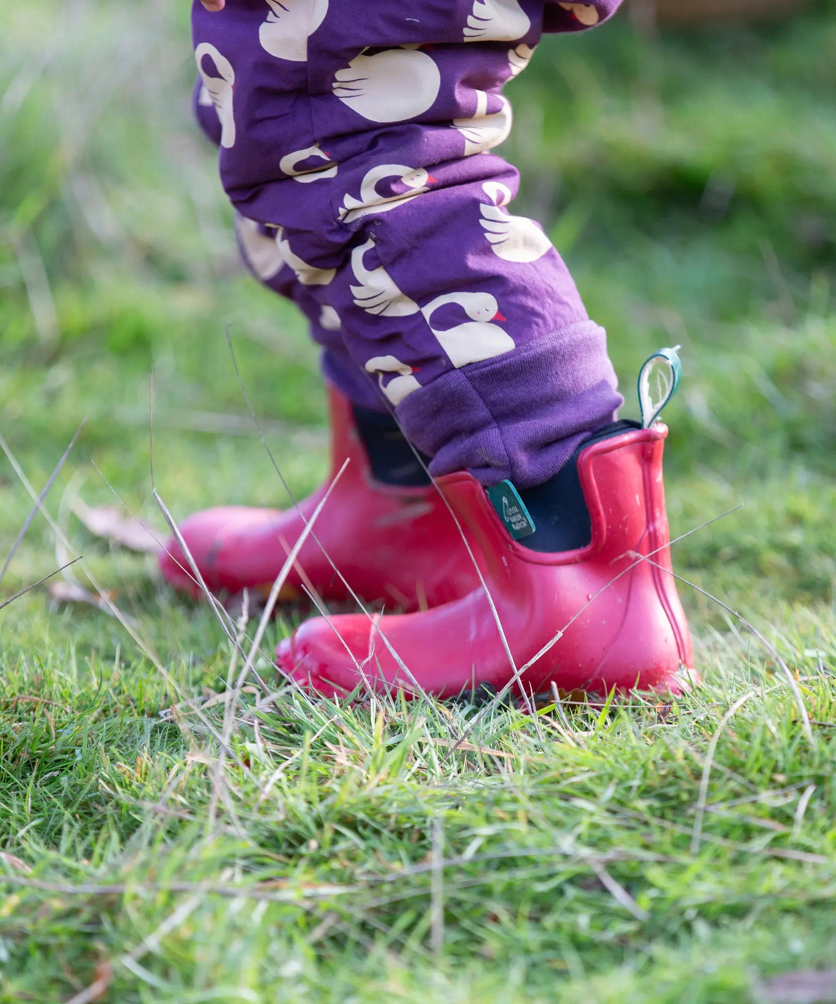 Close up of the leg cuffs on the Little Green Radicals purple sleeping swans print sherpa lined snowsuit worn by a child with red wellington boots.