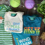 A flatlay featuring the four Little Green Radicals slogan playsuits. Three are folded up with one just off to the side laid out flat 
