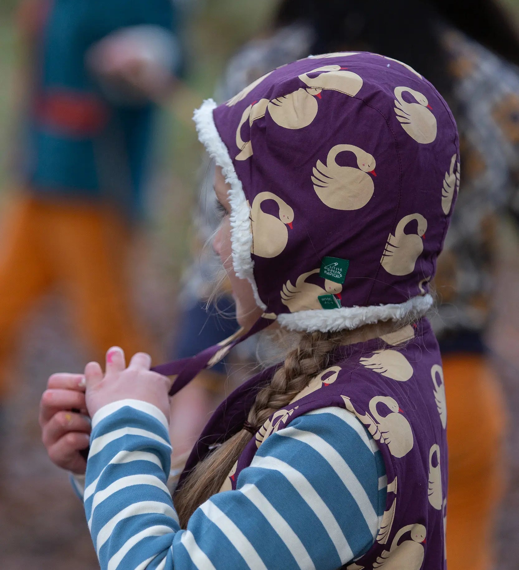 Child wearing the Little Green Radicals soft blue striped long sleeve t-shirt with purple sleeping swan filet and hat.