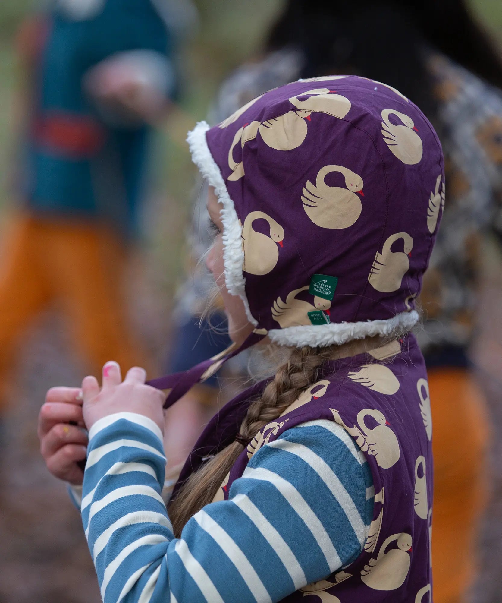 Child wearing the Little Green Radicals soft blue striped long sleeve t-shirt with purple sleeping swan filet and hat.