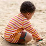 Back of a child wearing the Little Green Radicals sorbet striped UPF 50 sunsafe long sleeve rash vest with dark red swim shorts.