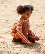 Child wearing the Little Green Radicals sorbet striped UPF 50 sunsafe long sleeve rash vest with yellow swim shorts. 