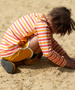 Child wearing the Little Green Radicals sorbet striped UPF 50 sunsafe long sleeve rash vest  with yellow swim shorts and wellington boots.