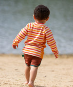 Back of child wearing the Little Green Radicals sorbet striped UPF 50 sunsafe long sleeve rash vest with dark red swim shorts.
