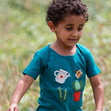 Child wearing the Little Green Radicals envelope neck Spring garden embroidered organic cotton green t-shirt. Features 4 embroidered elements, a white watering can, peas in their pods, a bee and a potted plant.