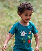 Child wearing the Little Green Radicals envelope neck Spring garden embroidered organic cotton green t-shirt. Features 4 embroidered elements, a white watering can, peas in their pods, a bee and a potted plant.