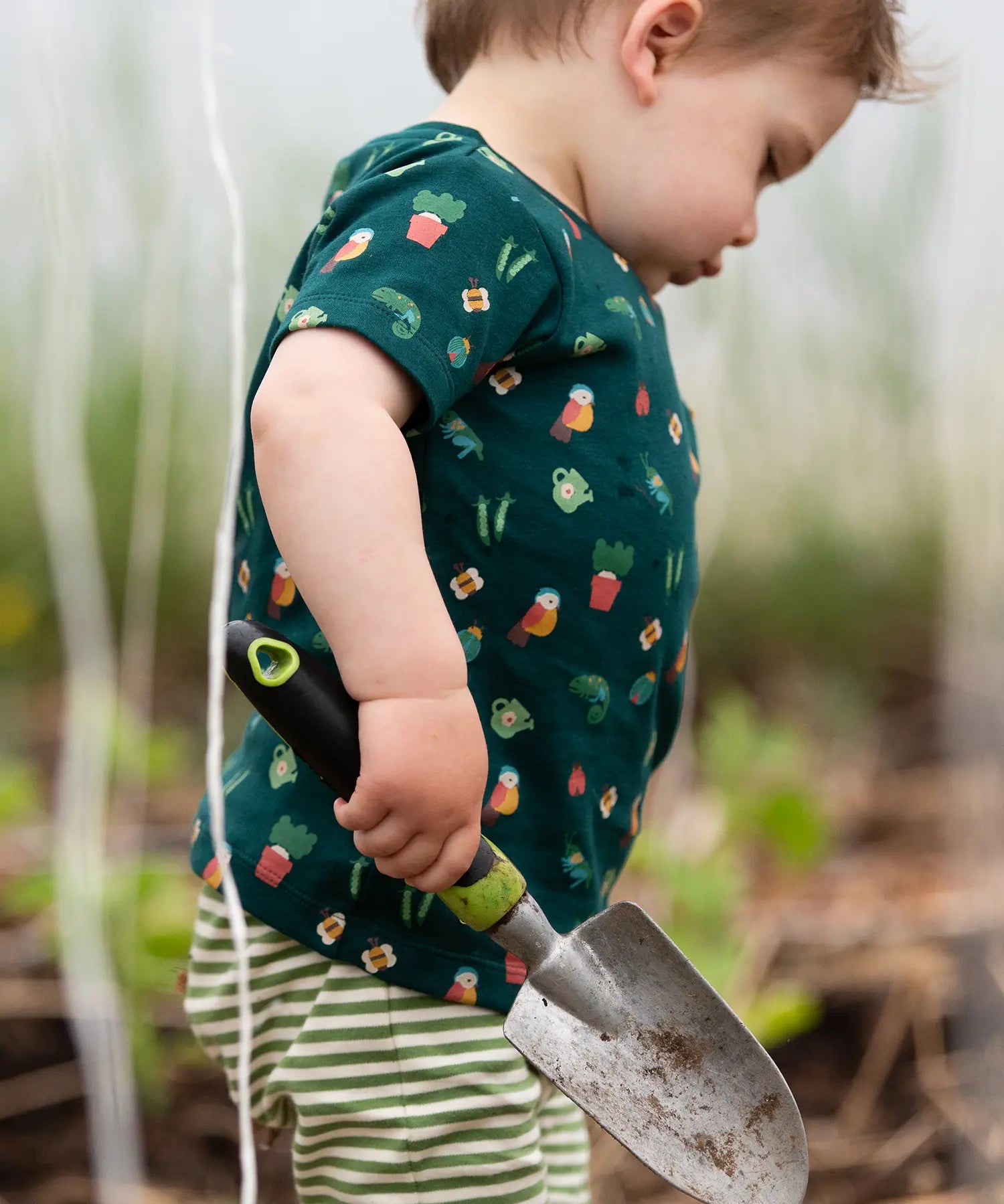Child wearing the Little Green Radicals Spring garden organic cotton playset outfit. Repeat pattern green t-shirt and green and cream striped joggers. 