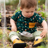 Child wearing the Little Green Radicals Spring garden organic cotton playset outfit with repeat pattern green t-shirt and green and cream striped joggers with yellow wellingtons. 