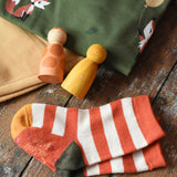 Orange and cream striped socks from the Little Green Radicals mushroom organic cotton socks 5 Pack placed on a wooden surface next to Maxomorra clothing and Grapat peg dolls.