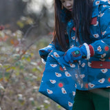 Child holding a Little Green Radicals  sun birds print blue recycled waterproof wet bag wearing a coat and gloves in the same print.