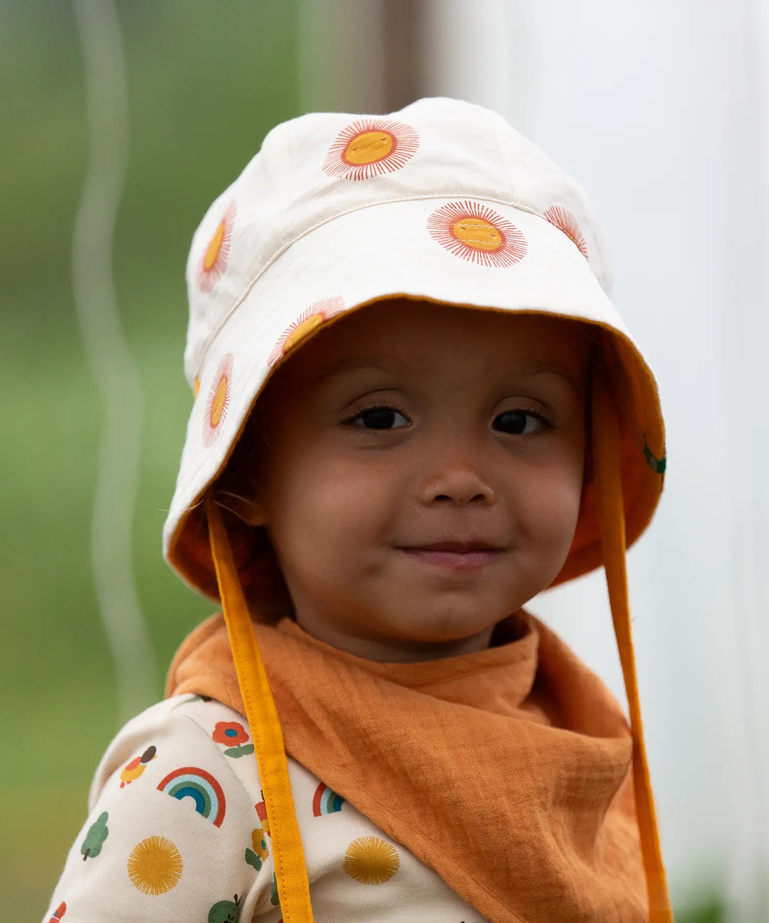 Child wearing the Little Green Radicals summer sun reversible cream sunhat on the repeat sun print side. 