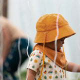 Child wearing the Little Green Radicals summer sun reversible cream sunhat on the ochre gold yellow side. 