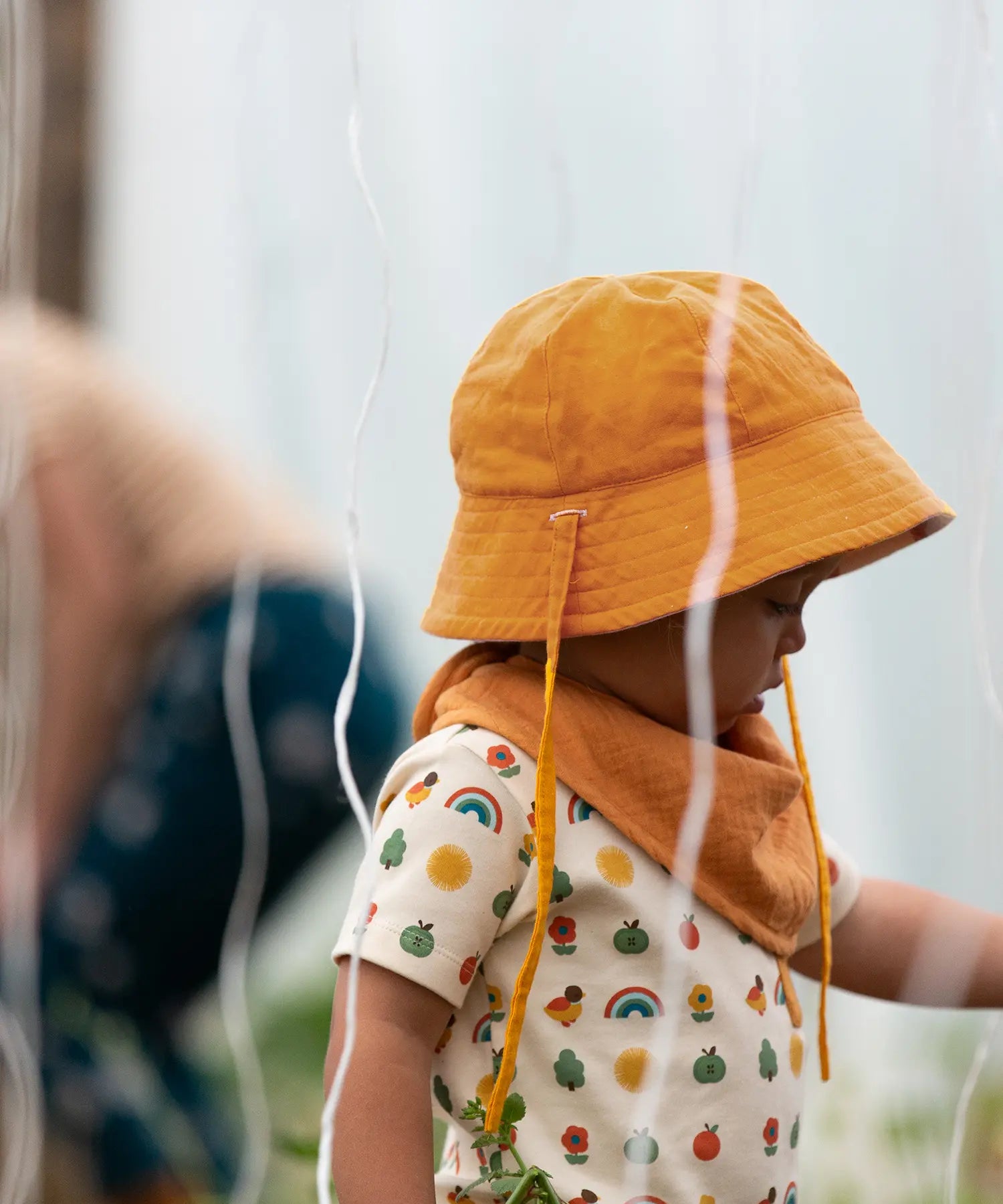 Child wearing the Little Green Radicals summer sun reversible cream sunhat on the ochre gold yellow side. 