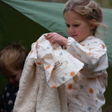 A child holding up the Little Green Radicals moon and sun print Organic Sherpa Hooded Baby Blanket in front of them showing off the fleecy side to the camera. The child is wearing matching pyjamas. This blanket is a part of a wide range of organic cotton clothing and accessories for children available here at Babipur. 
