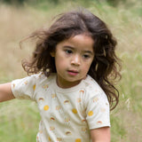 A child running, wearing the Little Green Radicals Sunshine & Rainbows Short Sleeve organic cotton T-Shirt. An off white, cream coloured t-shirt with an all over print featuring rainbows, sunshine and rainbow rainclouds. Little green Radicals have a wide range of organic cotton, Fairtrade children's clothing and outerwear available here at Babipur.