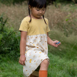Close up of girl walking in a grass field wearing the Little Green Radicals organic cotton sunshine and rainbows easy peasy dress