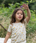 A child waving, wearing the Little Green Radicals Sunshine & Rainbows Short Sleeve organic cotton T-Shirt. An off white, cream coloured t-shirt with an all over print featuring rainbows, sunshine and rainbow rainclouds. Little green Radicals have a wide range of organic cotton, Fairtrade children's clothing and outerwear available here at Babipur.