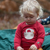 Child wearing the Little Green Radicals sleeping swan applique long sleeve organic cotton top in red with yellow gold joggers sitting on a dark green blanket outdoors.