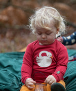 Child wearing the Little Green Radicals sleeping swan applique long sleeve organic cotton top in red with yellow gold joggers sitting on a dark green blanket outdoors.