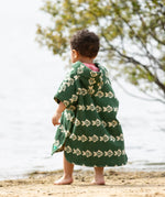 Little Green Radicals swimming fish organic cotton hooded towel poncho on child, view of back. Cream fish pattern on a green background.