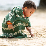 Child wearing the Little Green Radicals swimming fish organic cotton hooded towel poncho. Cream fish pattern on a green background.