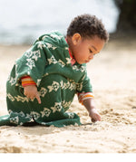 Child wearing the Little Green Radicals swimming fish organic cotton hooded towel poncho. Cream fish pattern on a green background.
