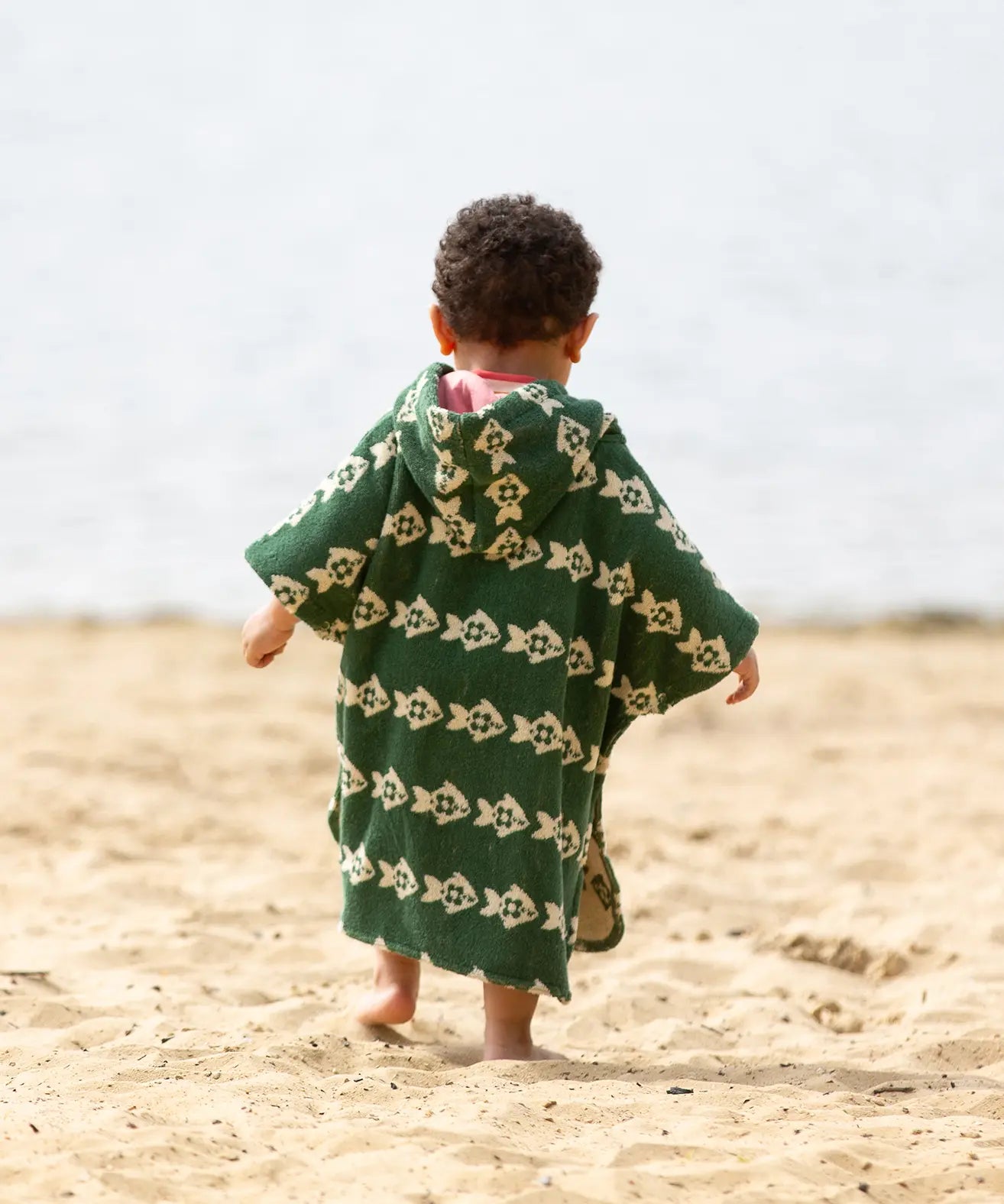 Little Green Radicals swimming fish organic cotton hooded towel poncho on a young child. Cream fish pattern on a green background. View of back