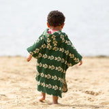 Little Green Radicals swimming fish organic cotton hooded towel poncho on a young child. Cream fish pattern on a green background. View of back
